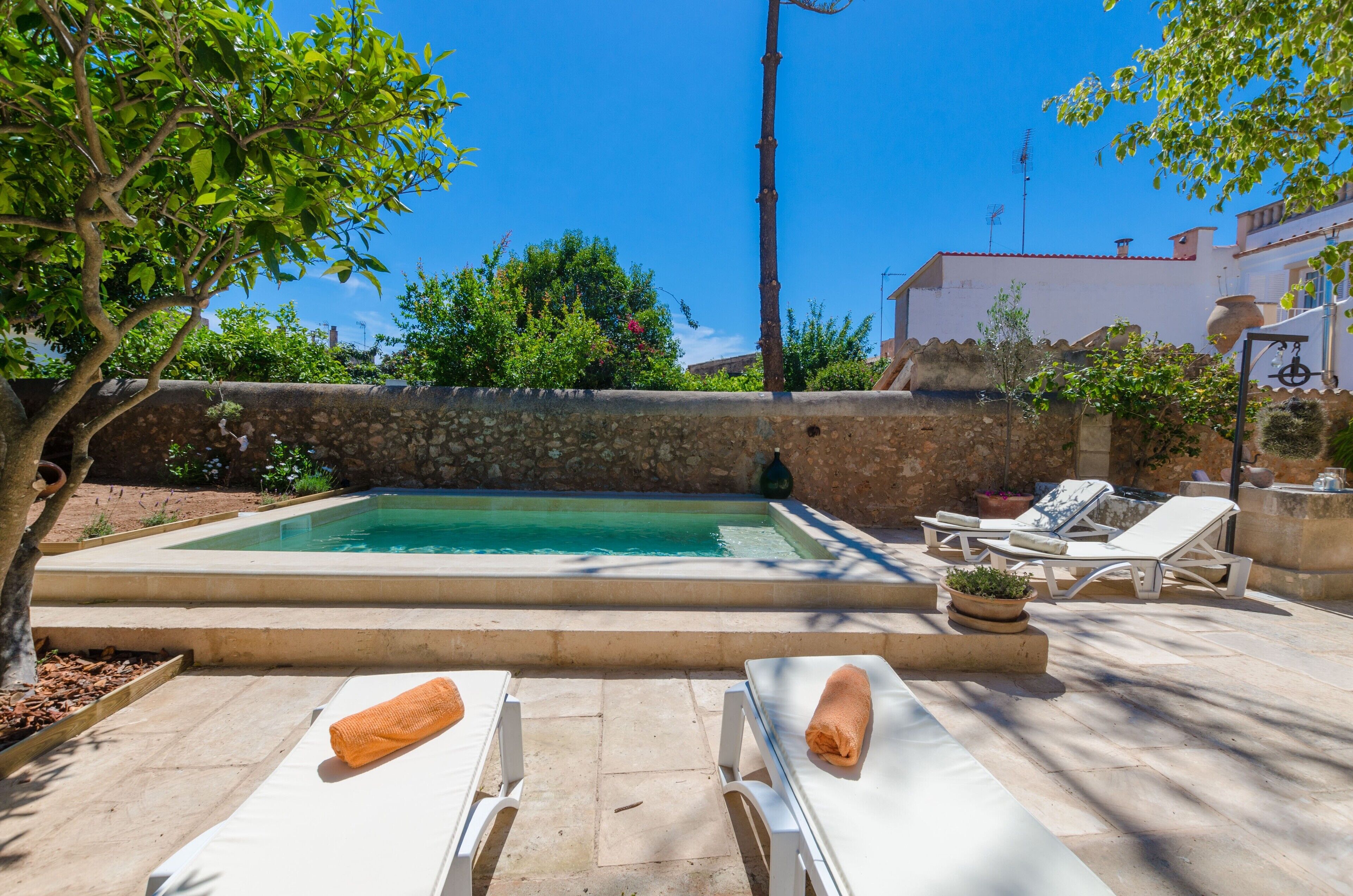 Piscina con sillas de descanso y una pared de piedra.