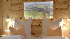A wooden cabin room with a bed featuring white bedding and two large pillows. A window provides a view of a green landscape. - (2) Ferienwohnung 35 qm mit Balkon (Reit im Winkl)