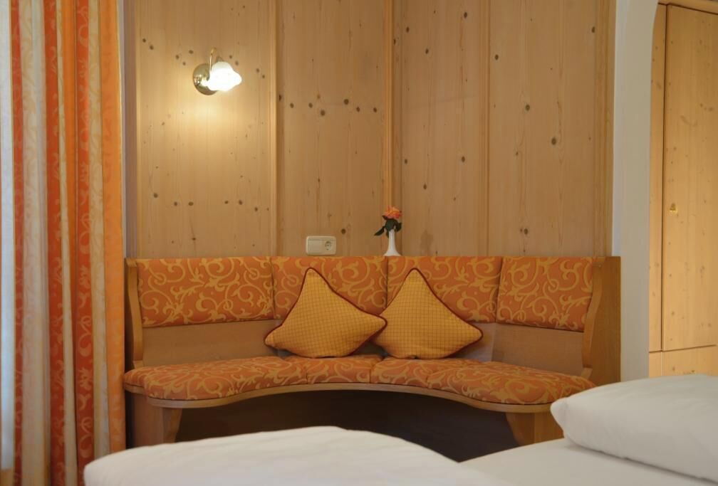 Una habitación con pared de paneles de madera, un banco con cojines estampados, una mesita con un jarrón y una cama con ropa blanca.