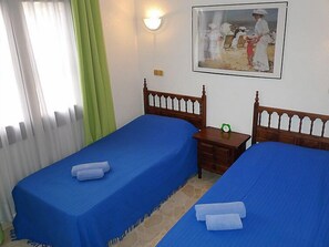 A room with two single beds, a nightstand, a green clock, and a painting on the wall.