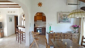 Een ruime eethoek met een hoge tafel en meerdere stoelen, een keuken met houten kastjes, en een groot raam.