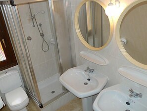 A bathroom with a glass-enclosed shower, a pedestal sink, a vanity mirror, and a toilet.