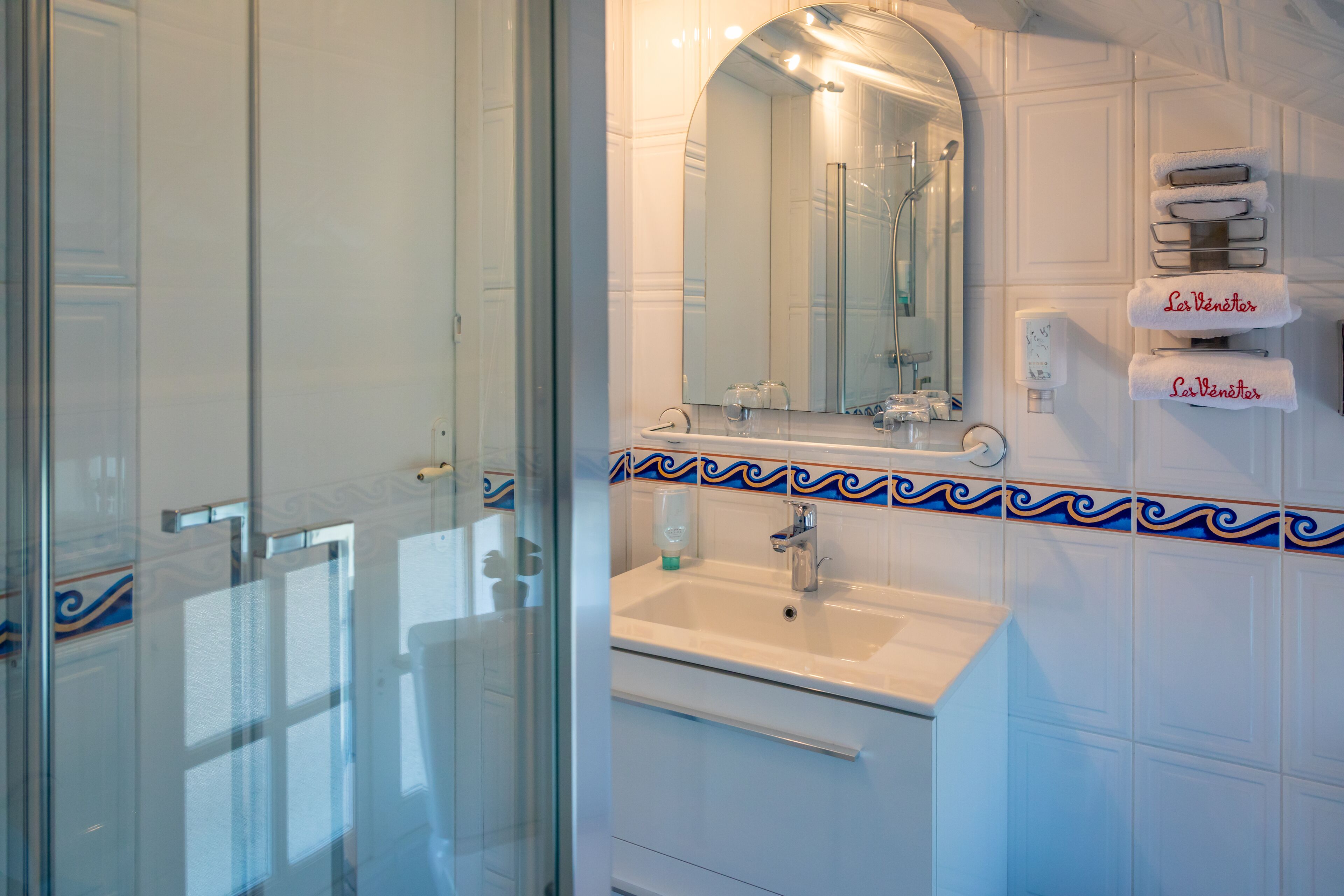 Un baño con puerta de vidrio para la ducha, un lavabo con espejo y un perchero con toallas.