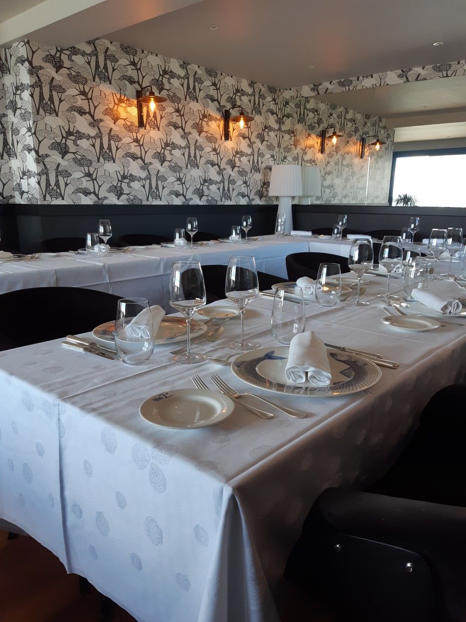 Un espace repas avec des tables dressées pour le repas, agrémenté d’un papier peint à motifs et d’un éclairage mural.