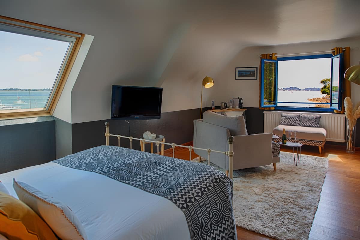 A bedroom with a large bed, a TV, a desk, and a view of the sea.
