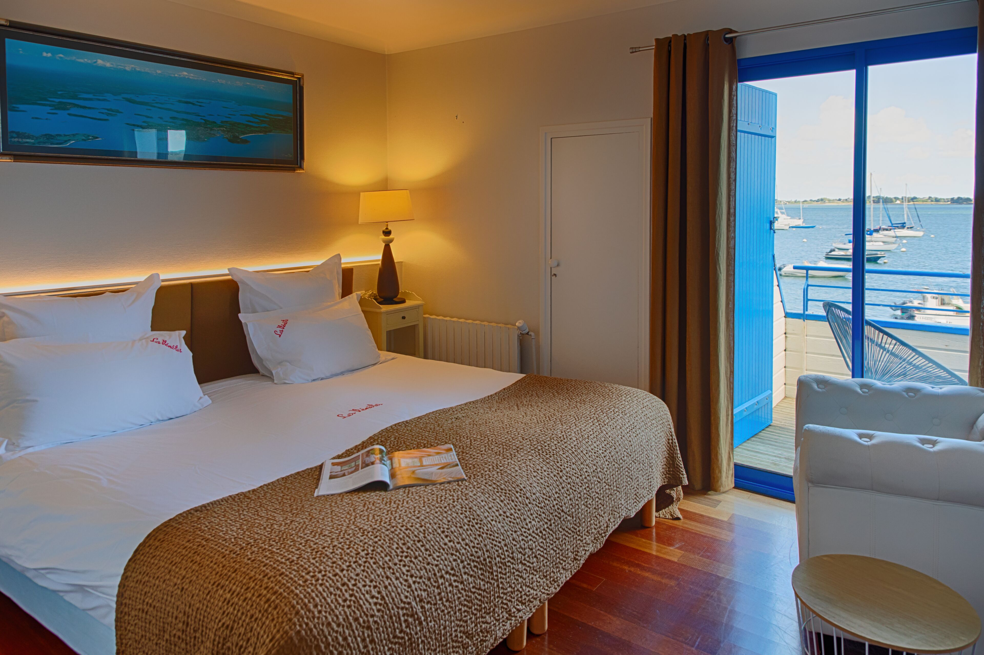 Ett hotellrum med en stor säng, en läslampa, utsikt över båtar från balkongen och en stol.