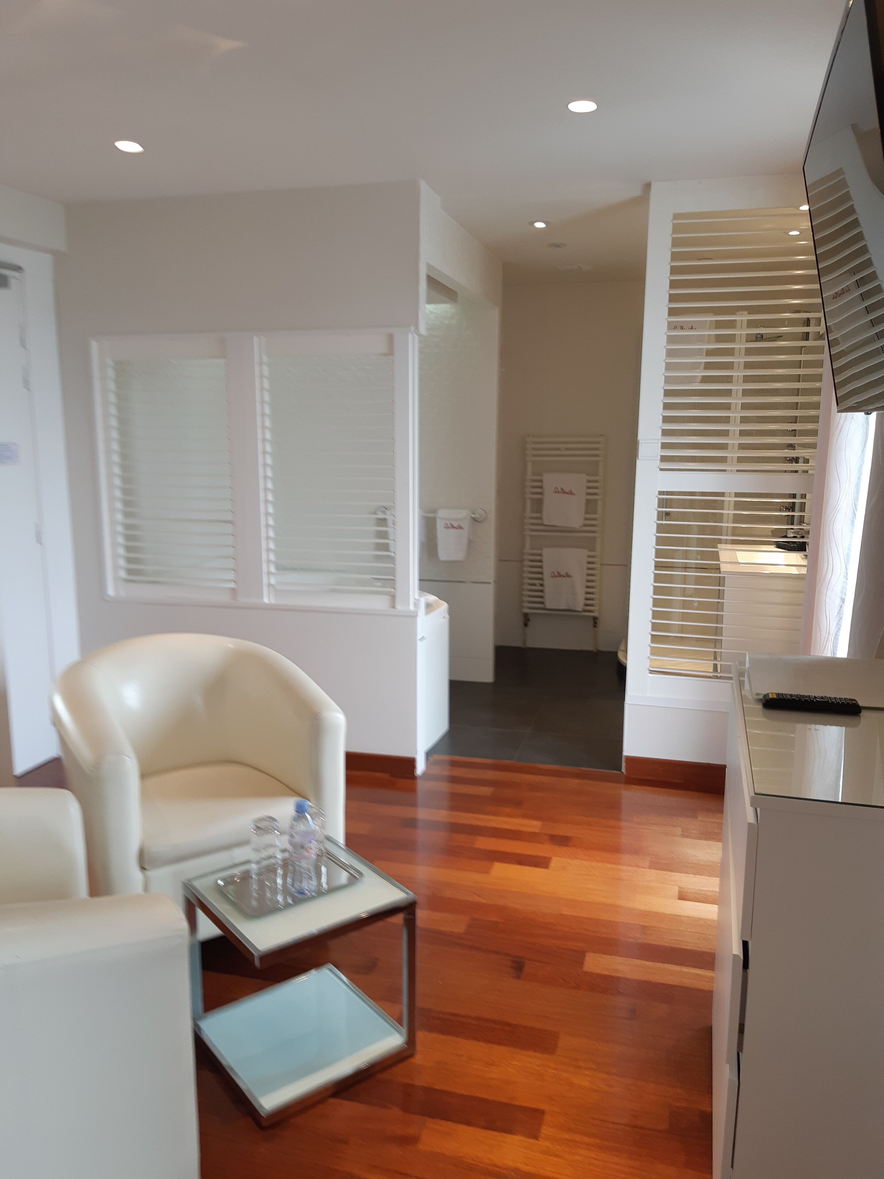 Una sala de estar moderna con un sillón blanco, una mesa de centro de vidrio, piso de madera, un armario blanco y un televisor sobre un mueble.