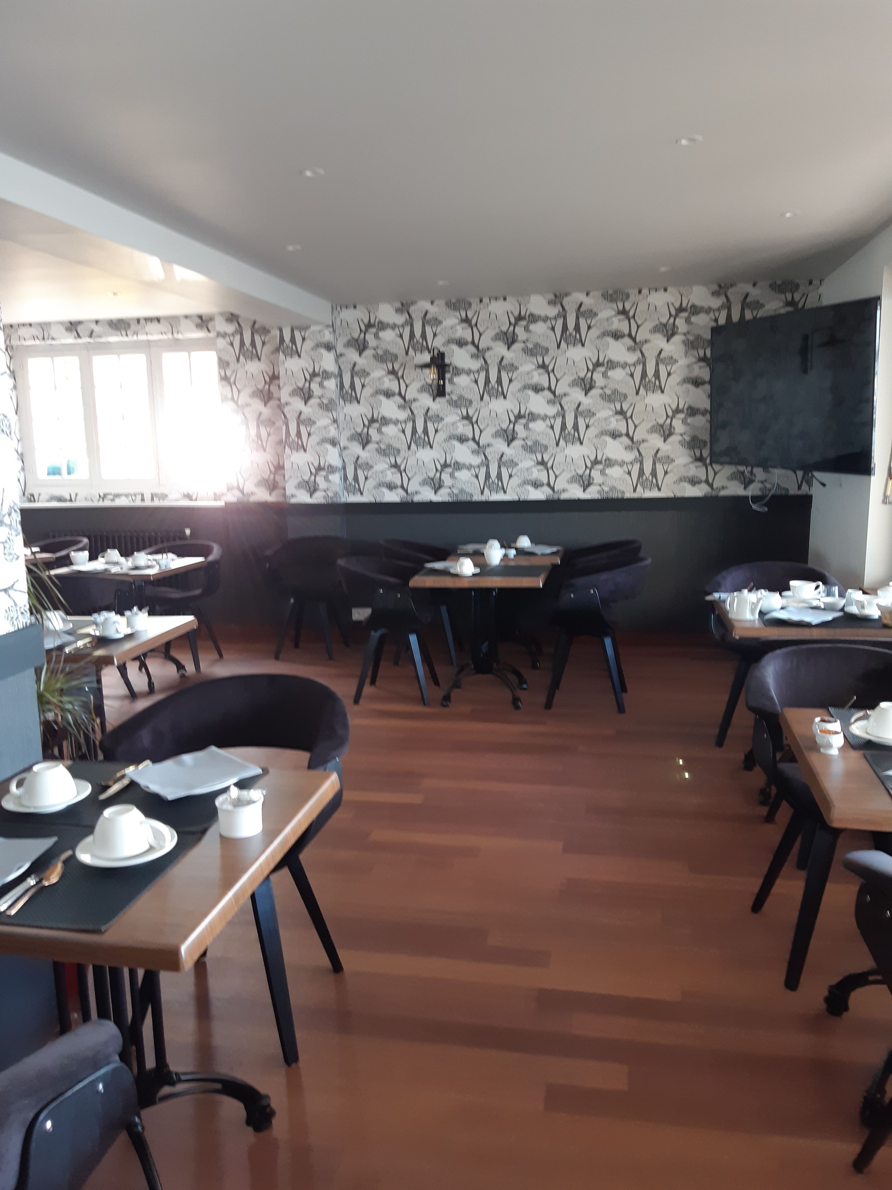 Un comedor con varias mesas y sillas, un muro con diseño y un televisor montado.