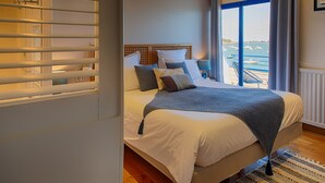 Un dormitorio con una cama grande, vista al puerto deportivo por la ventana y un balcón con barandilla.