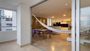 A modern interior with a dining area, a hammock, and a kitchen visible through a glass door.