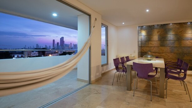 A modern dining area with a city view, a glass table, and purple chairs.