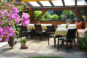 An outdoor patio with wooden tables and chairs, surrounded by potted plants and a view of greenery. - (3) Ferienwohnung 31 qm mit Balkon (Reit im Winkl)