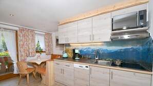 Ett kompakt kök med träskåp, en inbyggd mikrovågsugn och utsikt över bergen genom en glasvägg.