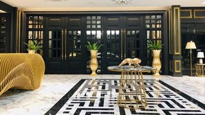 A lobby with a black and white patterned floor, a round table with a gold base, and two potted plants. - Belle Grand Hotel (Udon Thani)