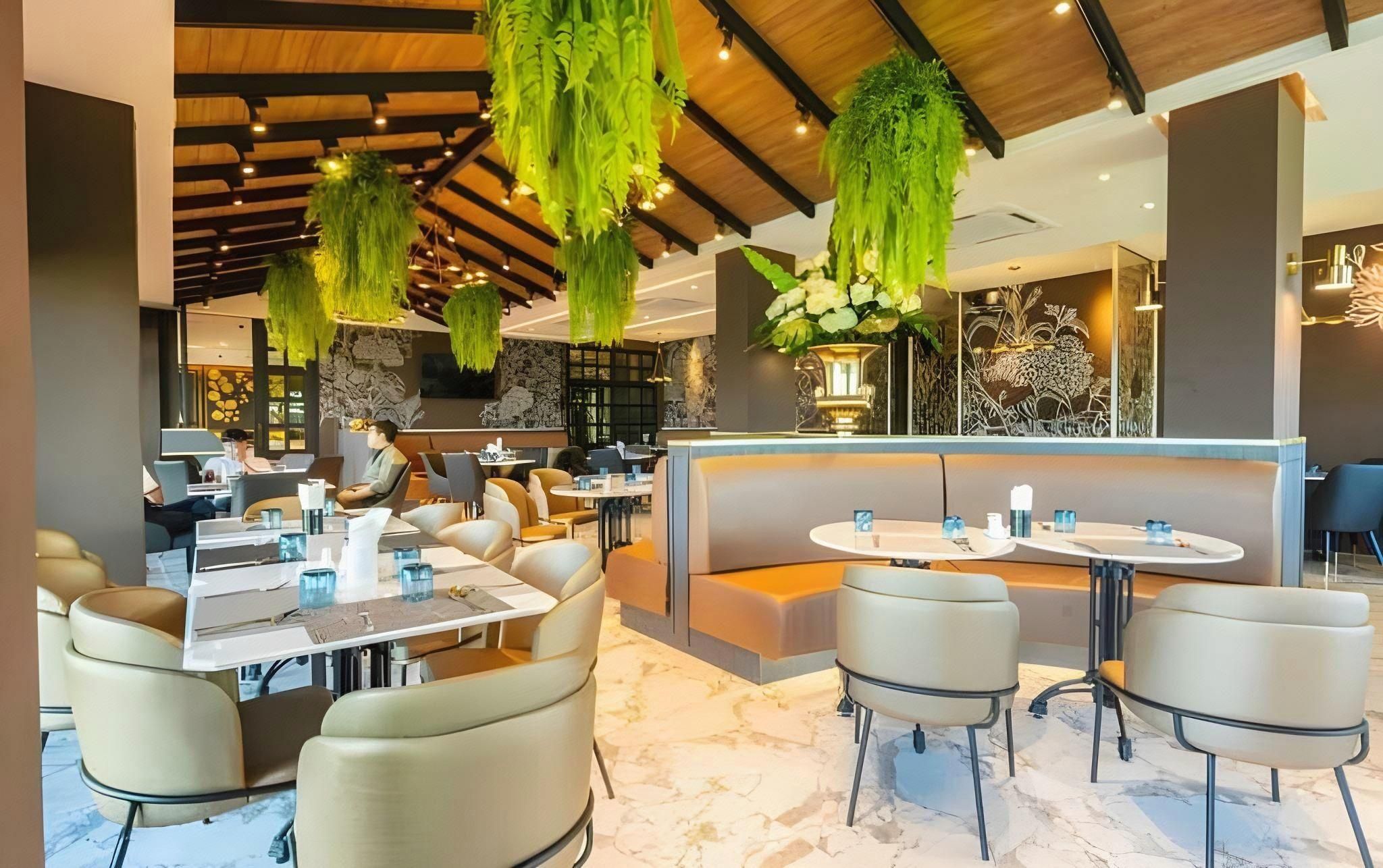 A modern restaurant interior with hanging greenery, marble flooring, and contemporary furniture.