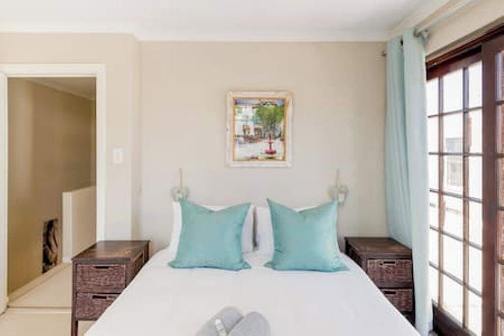 A bedroom with a bed, two pillows, a nightstand, a window, and a door.