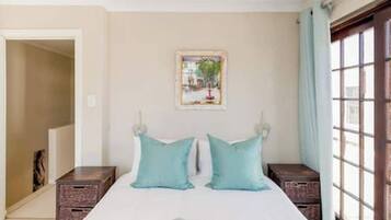 A bedroom with a bed, two pillows, a nightstand, a window, and a door.