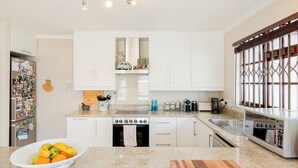 Una cocina moderna con armarios blancos, horno empotrado, un lavabo y un bol con fruta en la encimera.