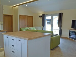 Una sala de estar moderna con un sofá verde, armarios de madera, una isla de cocina y un televisor.