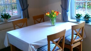 Une salle à manger avec une table mise pour quatre personnes, des chaises en bois, un vase de fleurs et une horloge au mur.