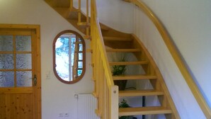 Un escalier en bois avec une rampe, une porte dotée de panneaux en verre dépoli et un radiateur fixé au mur.
