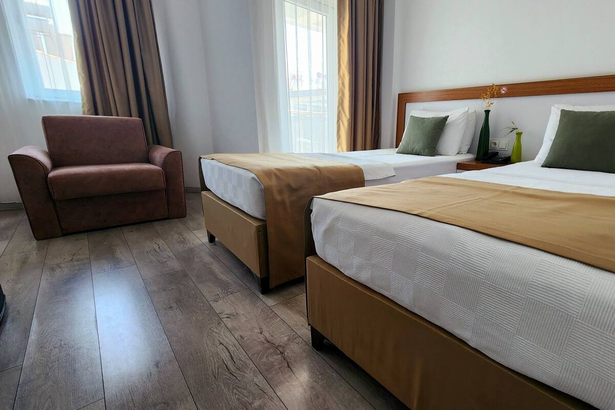 A hotel room with two beds, a brown leather armchair, and a wooden headboard.