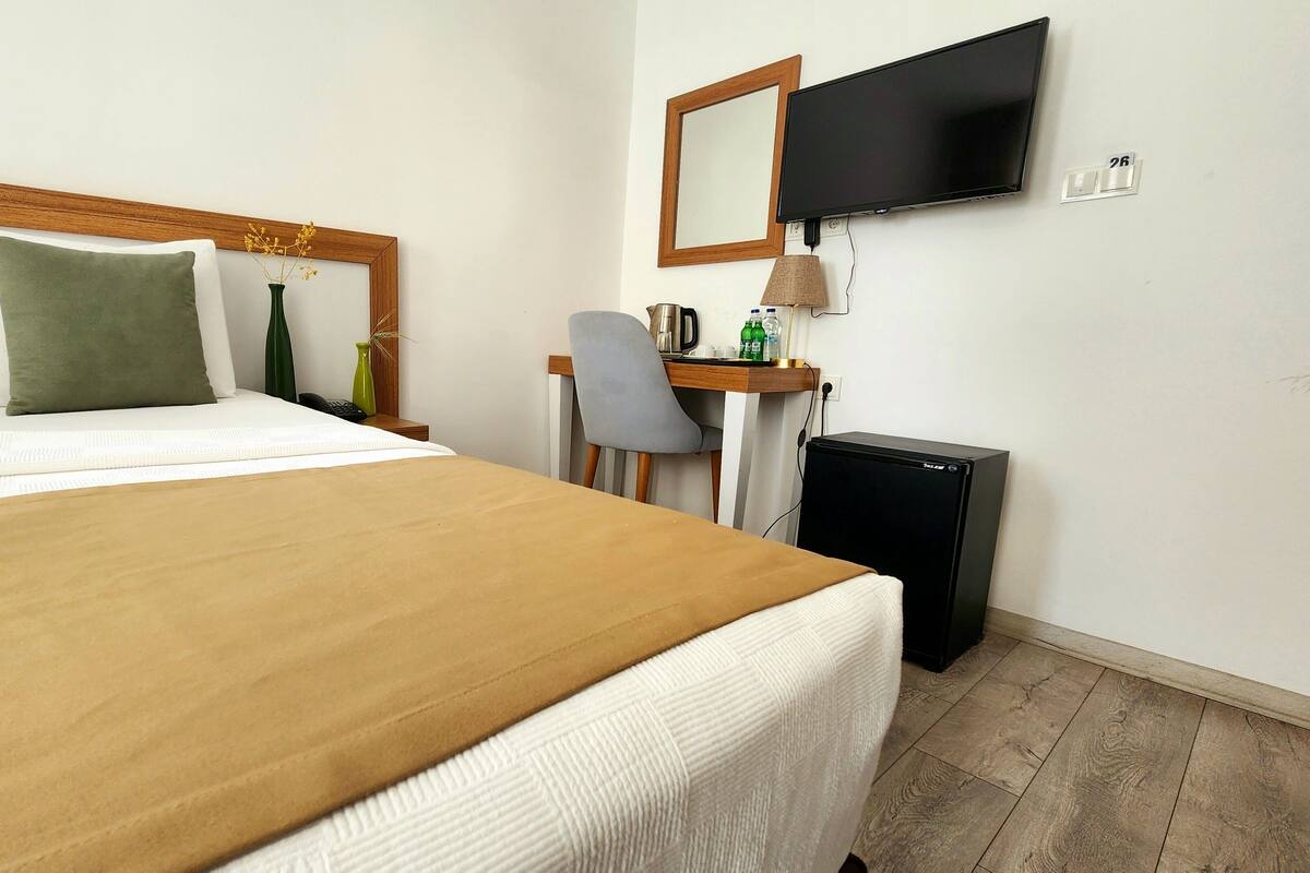 A hotel room with a bed, a desk, a chair, a television, and a refrigerator.