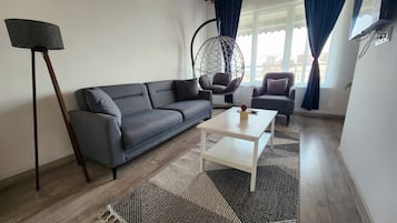 A living room with a grey sofa, a white coffee table, a hanging chair, and a small table with a pineapple decoration.