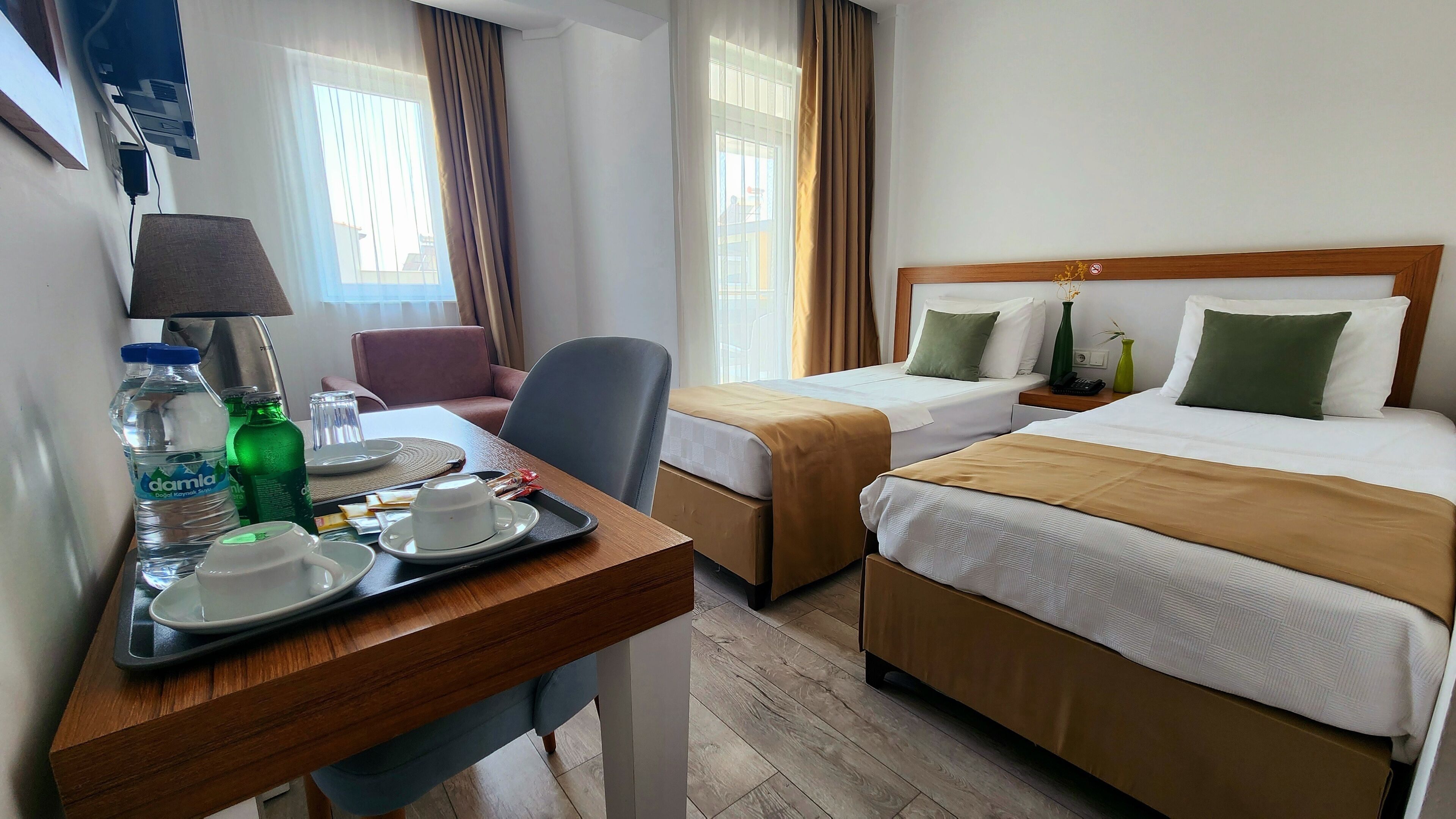 A hotel room with two beds, a desk with a chair, a TV, and a window with curtains.
