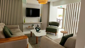 A modern living room with a flat-screen TV, a sofa, a chair, a small table, and a hanging light fixture. - Karden Otel (Antalya)