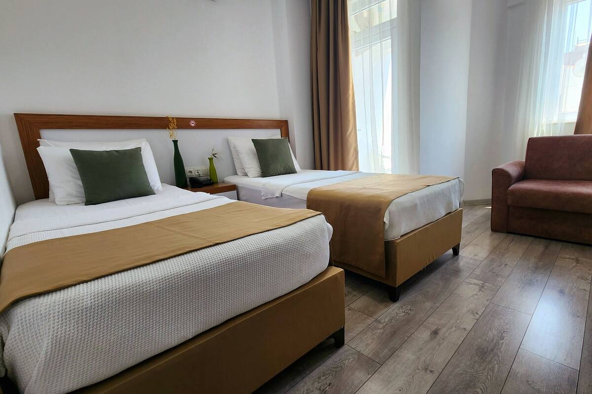 A hotel room with two beds, a wooden headboard, a brown chair, and a wooden floor.