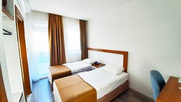 A hotel room with two beds, a wooden headboard, a desk, and a window with curtains.