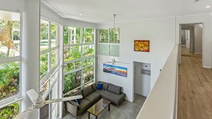 Un vaste espace de vie doté de grandes fenêtres, d’un ventilateur de plafond et d’un canapé moderne.