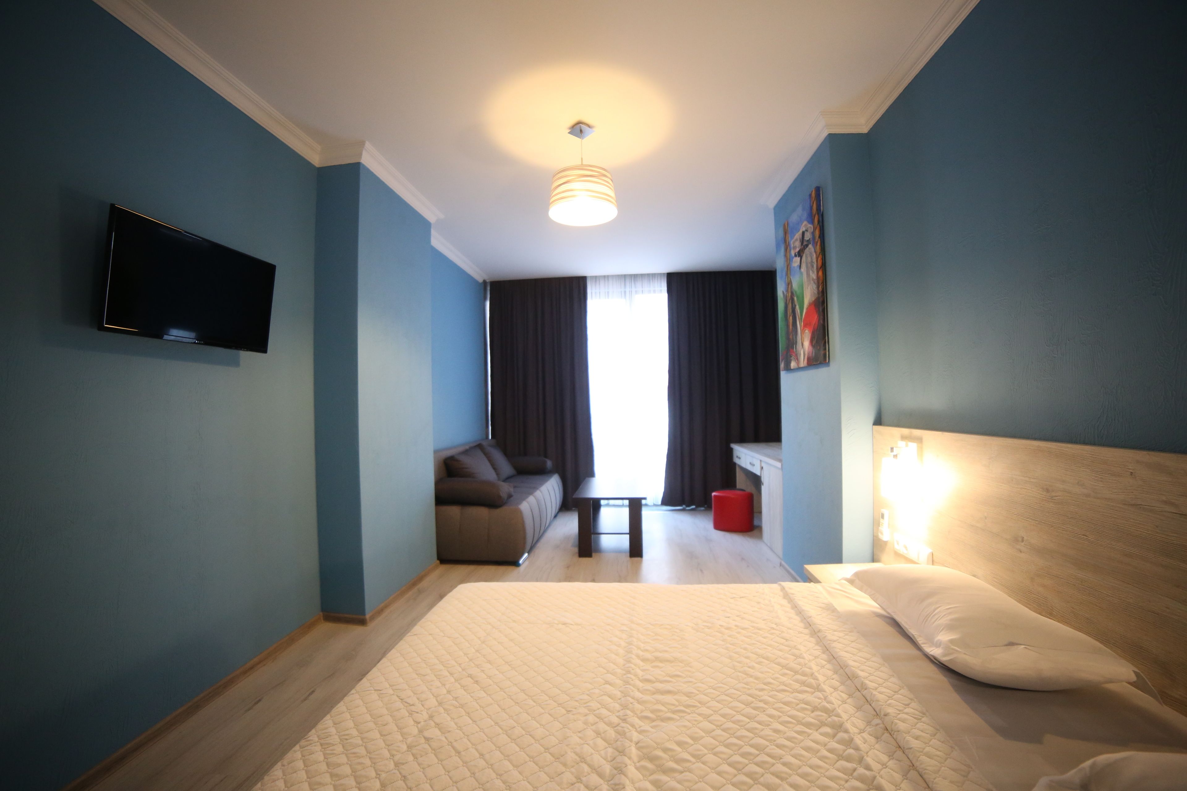 Een hotelkamer met een bed, een aan de muur bevestigde televisie, een bank, een klein tafeltje en een schilderij.
