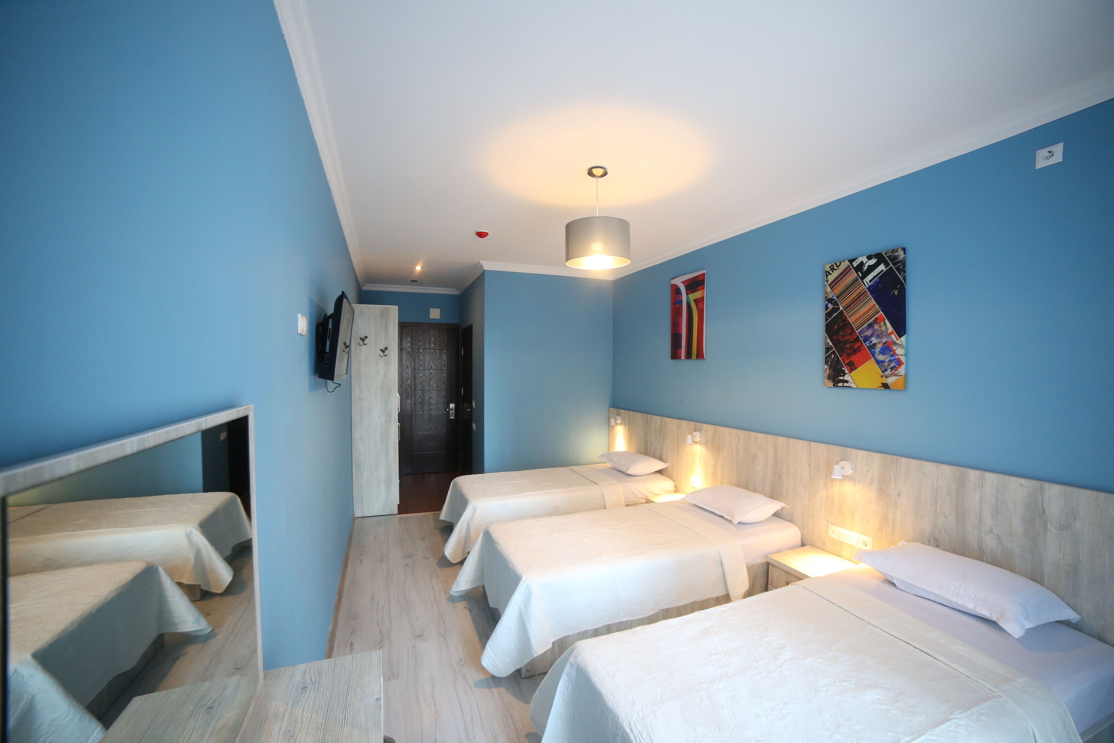 A hotel room with four single beds, a wooden headboard, a wall-mounted TV, and a door leading to a bathroom.