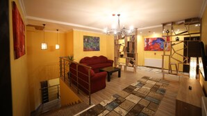 A living room with a red sofa, a coffee table, a chandelier, and a staircase. - Hotel Soft (Batumi)