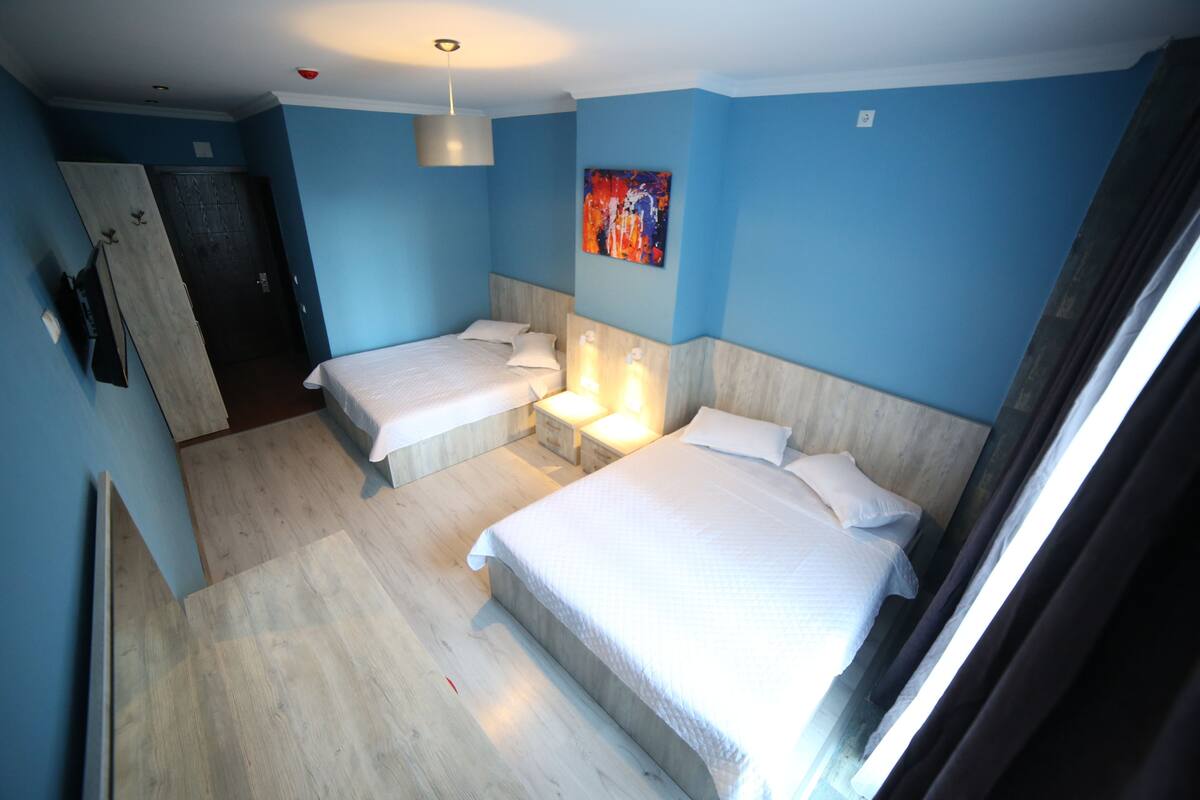 A hotel room with two beds, wooden flooring, a blue wall, and a painting.