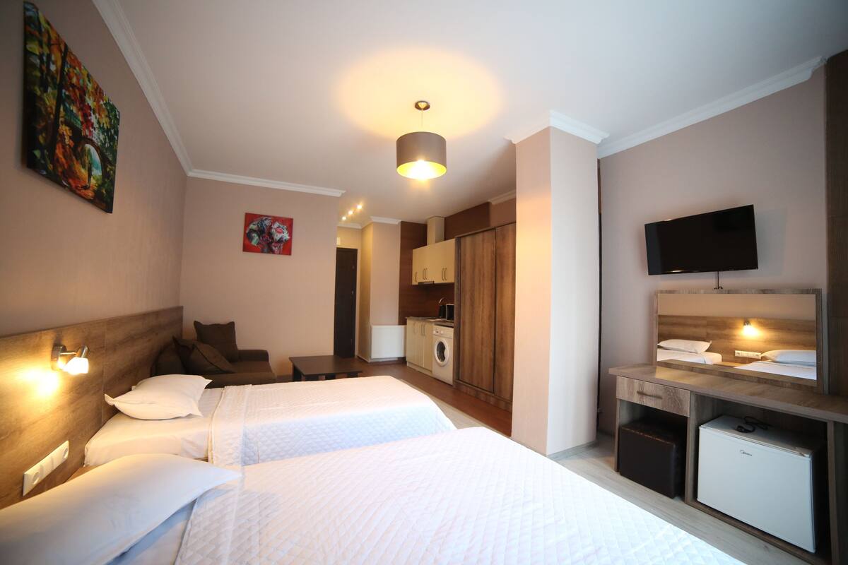 A hotel room with two beds, a TV, a washing machine, and a small kitchenette.