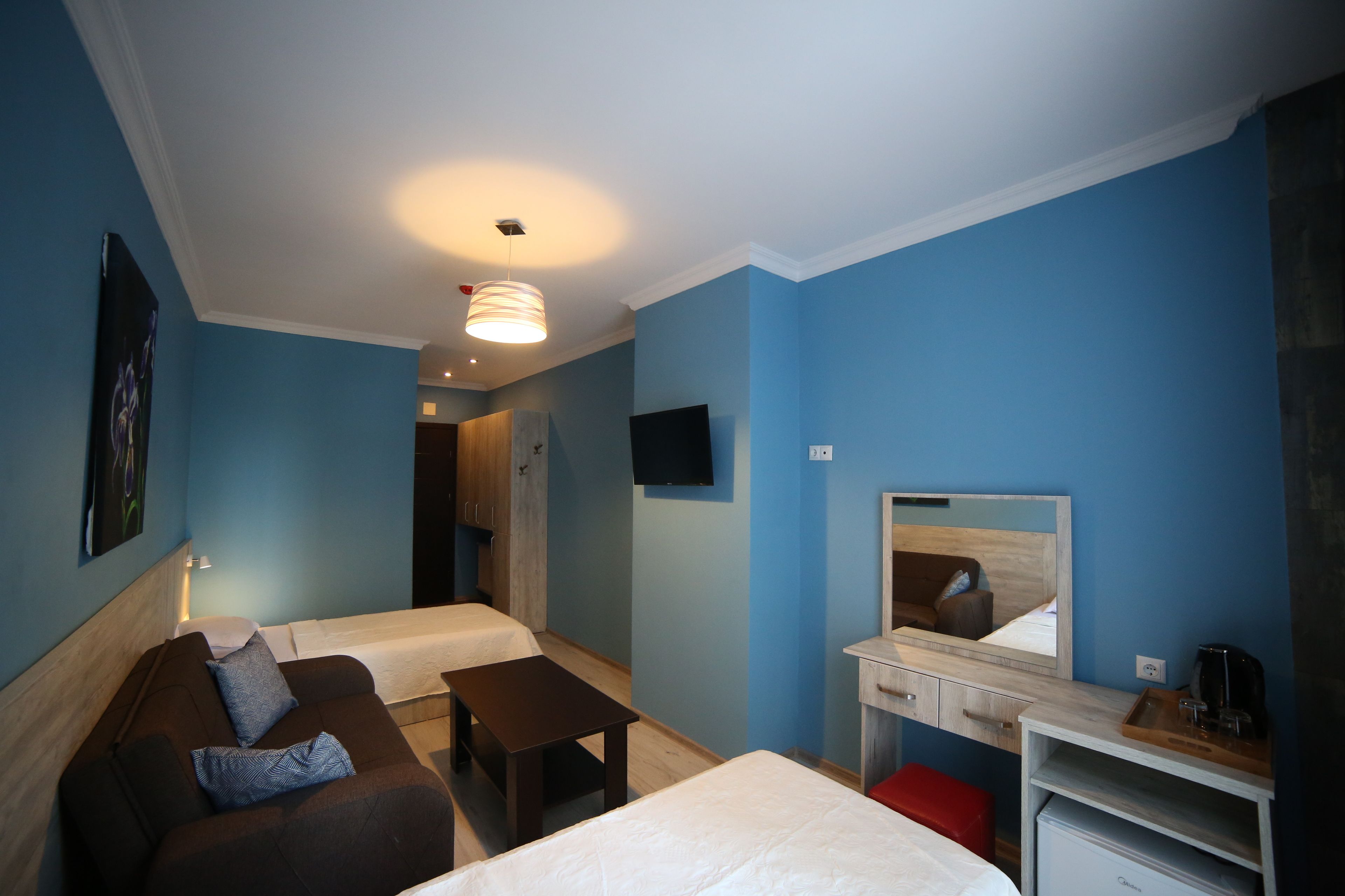 Habitación de hotel con dos camas, un escritorio, un espejo, un televisor y una pequeña kitchenette.