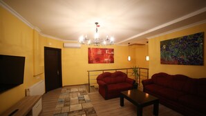 A living room with two red sofas, a wooden coffee table, a TV on the left, and a painting on the wall. - Hotel Soft (Batumi)