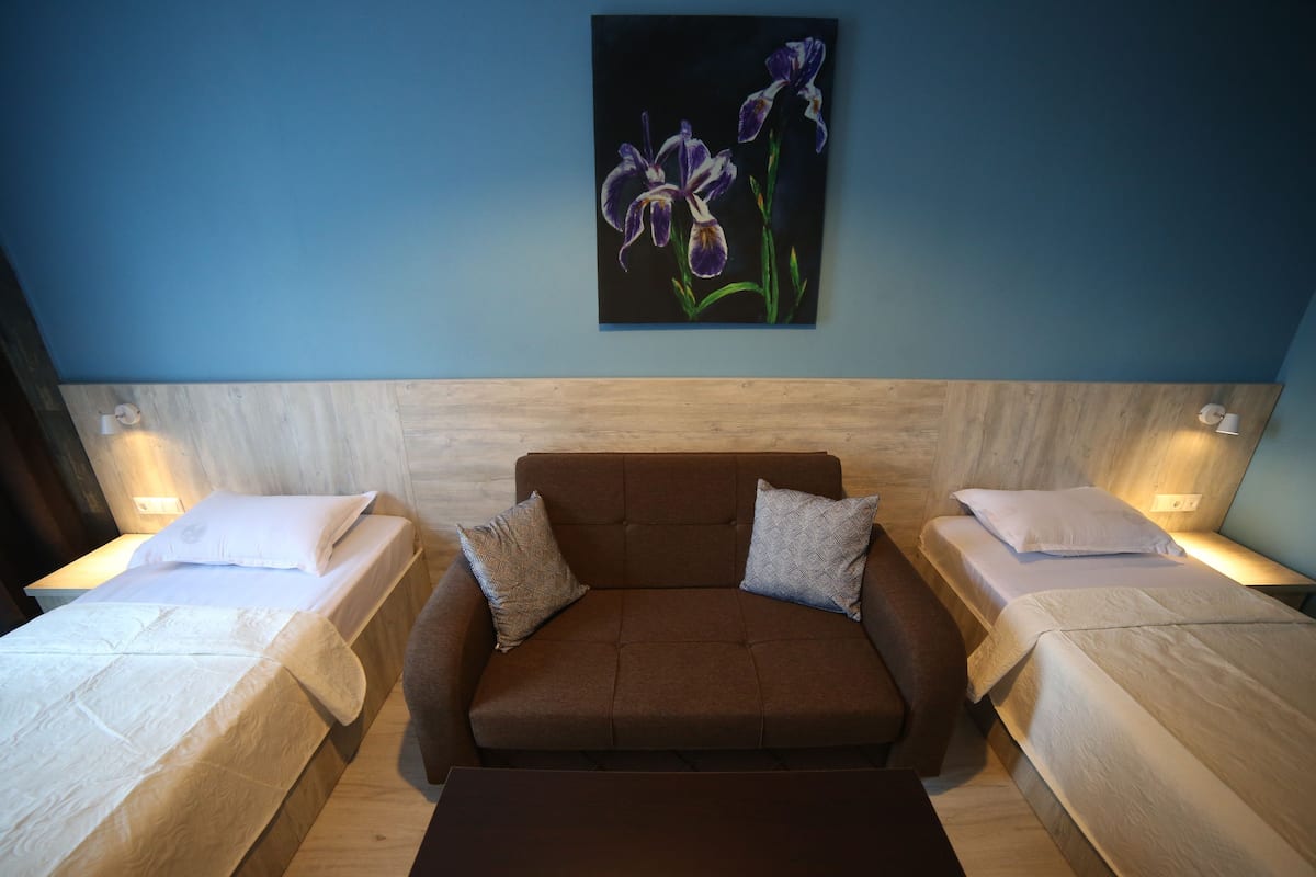 A hotel room with a brown sofa, two single beds, and a painting of flowers on the wall.