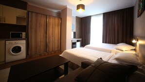 A hotel room with a washing machine, a bed, a desk, and a hanging light fixture. - Hotel Soft (Batumi)