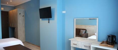 Una habitación de hotel con cama, escritorio con espejo, televisor y armario.