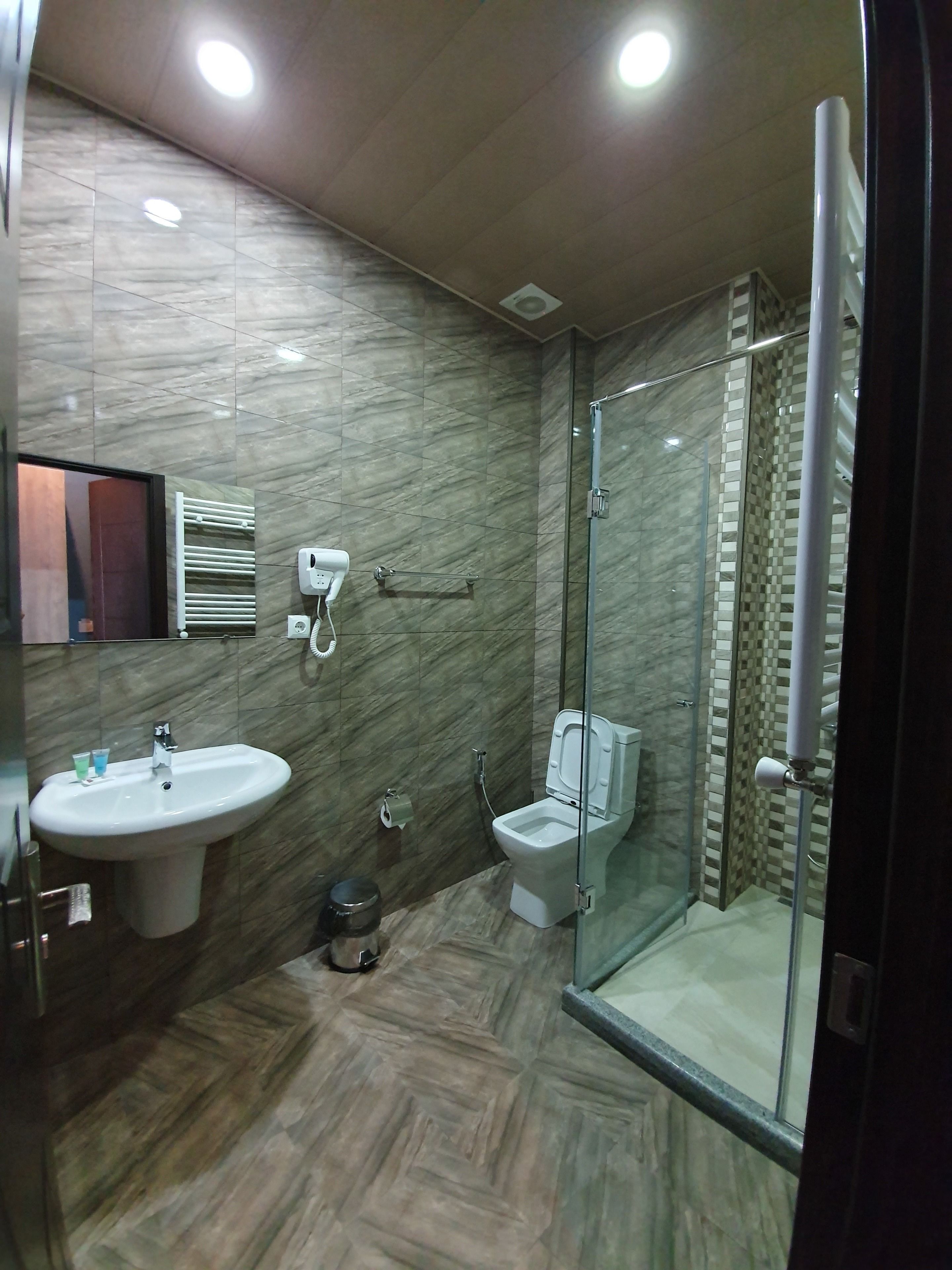 A modern bathroom with a marble floor, a sink, a toilet, and a glass-enclosed shower area.