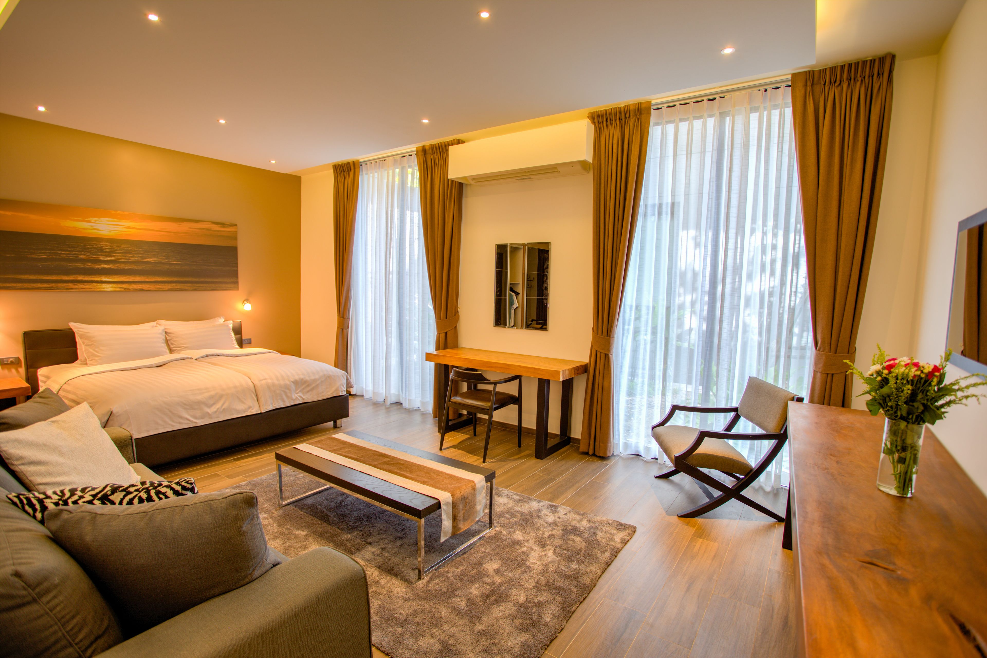 A modern hotel room with a large bed, a sofa, a dining table, and a chair.