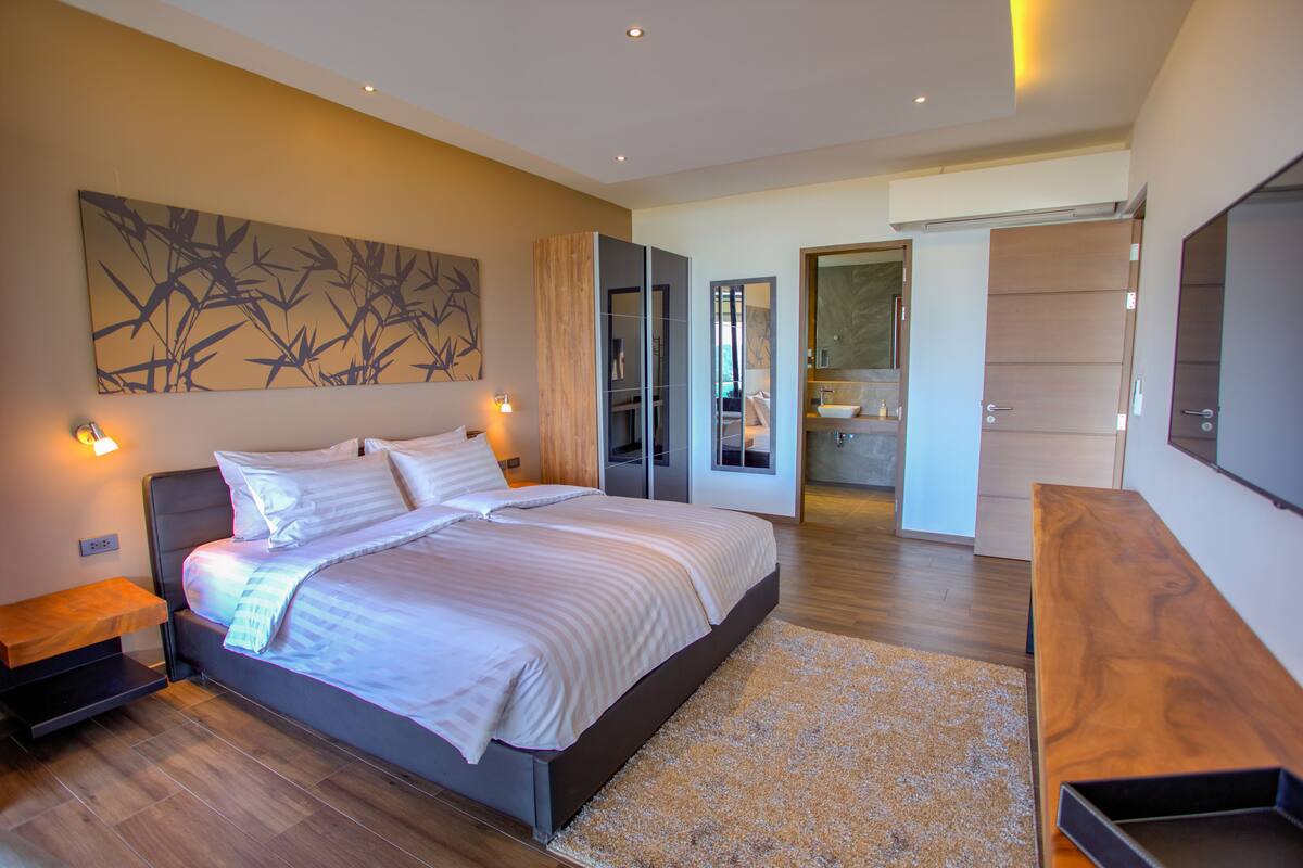 A modern bedroom with a large bed, bedside tables, a wooden bench, and a large mirror.