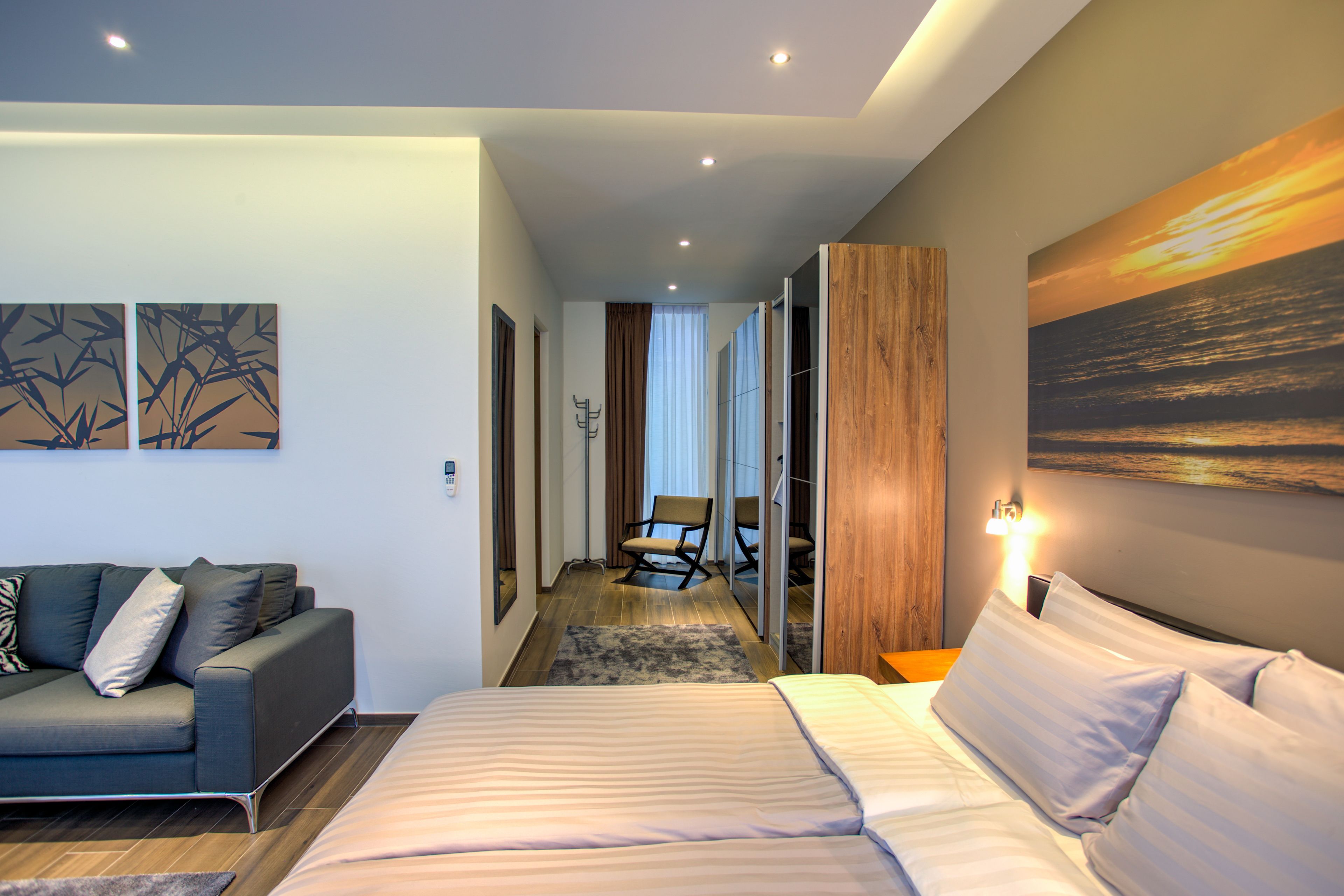 Una habitación de hotel moderna con una cama, un sofá y un cuadro de una puesta de sol.