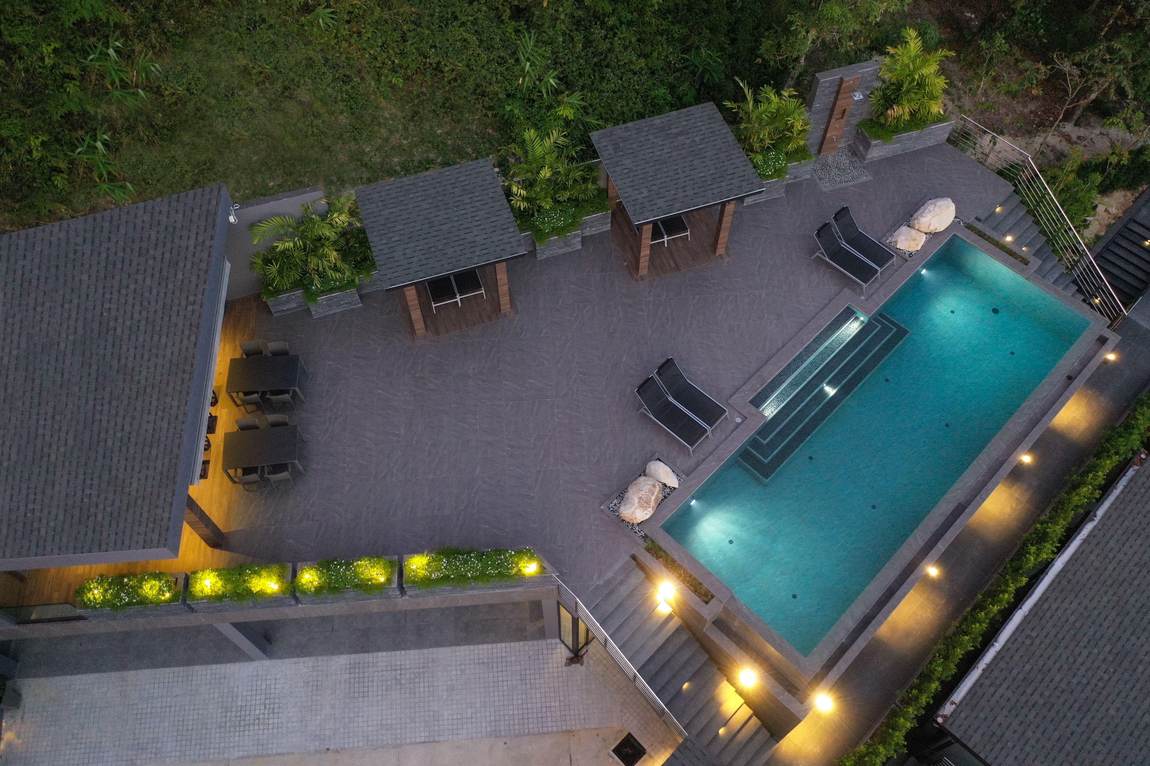 An aerial view of a resort with a swimming pool, lounge chairs, and a covered seating area.