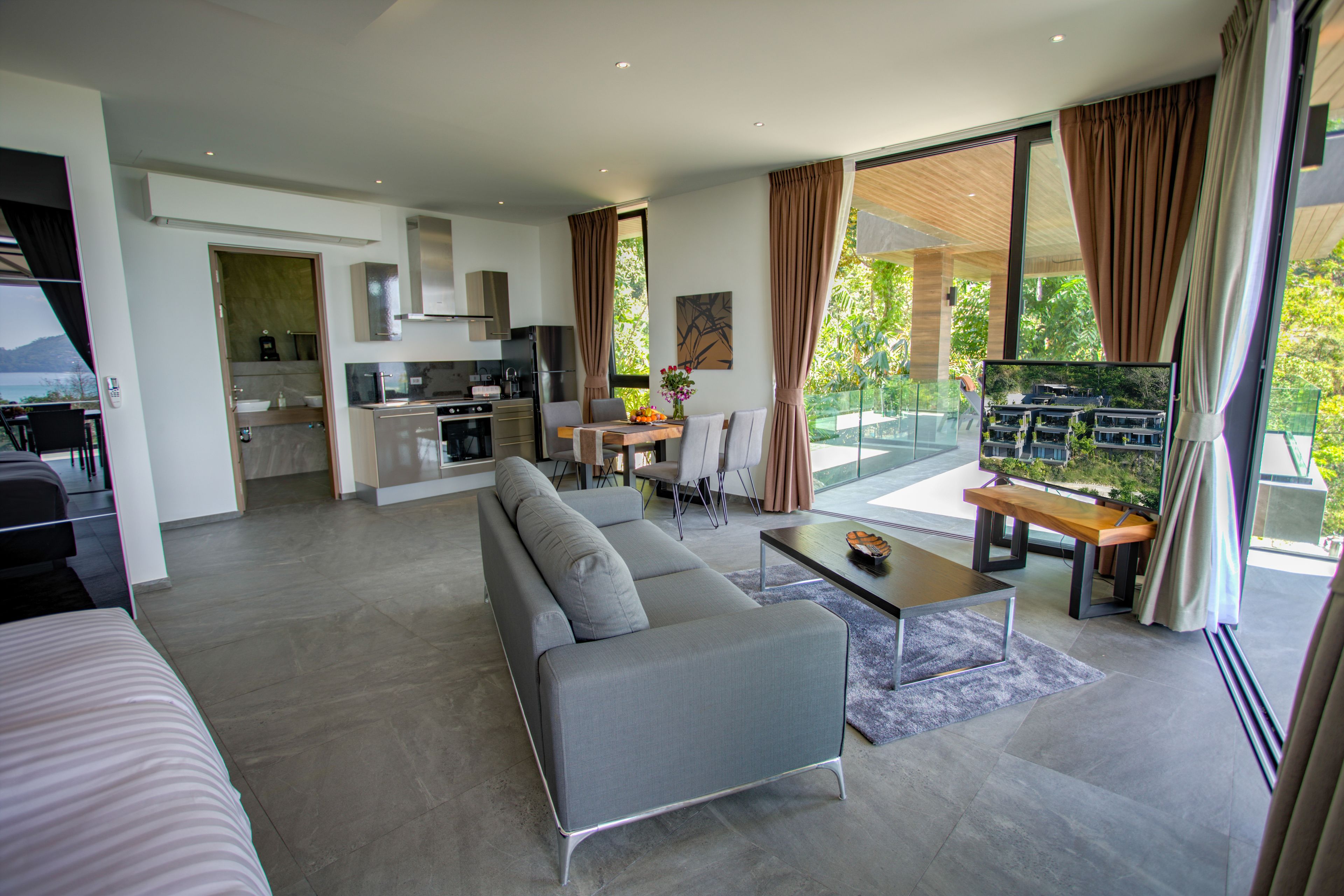 A modern living room with a grey sofa, a dining table with chairs, and a kitchen area in the background.