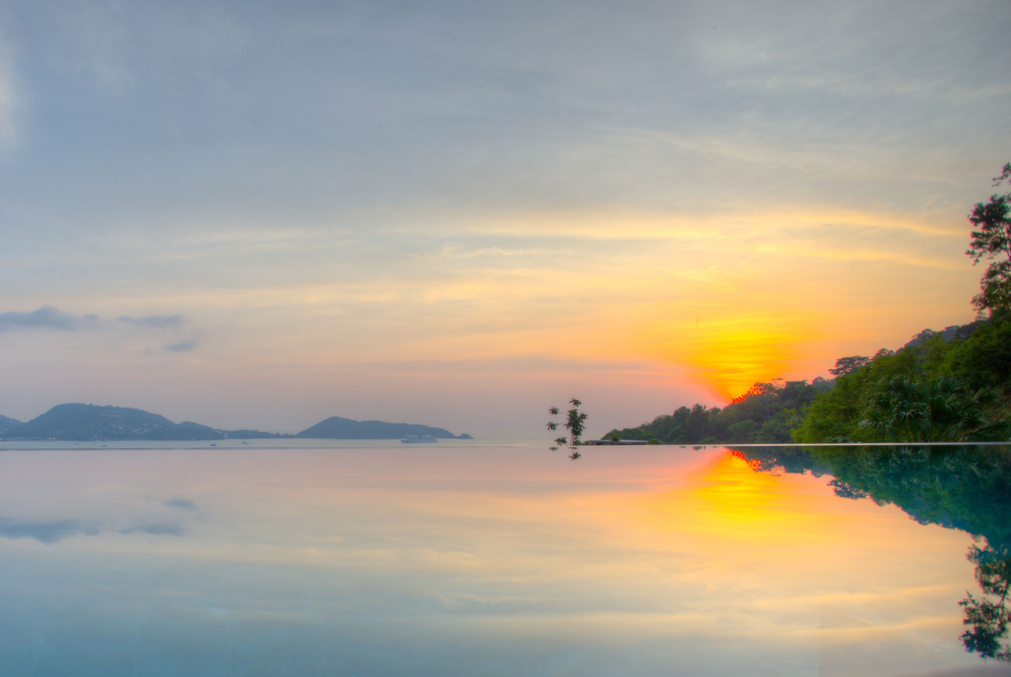 A calm lake with a sunset, clear sky, and distant mountains.
